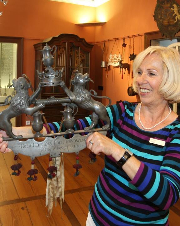  [Translate to Englisch:] Eine Museumsführerin präsentiert ein Stück aus der Zinn-Sammlung des Weygang-Museums in Öhringen.